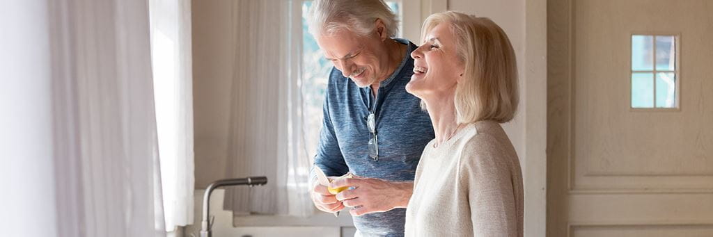 A senior couple laughs while preparing a meal in their home.