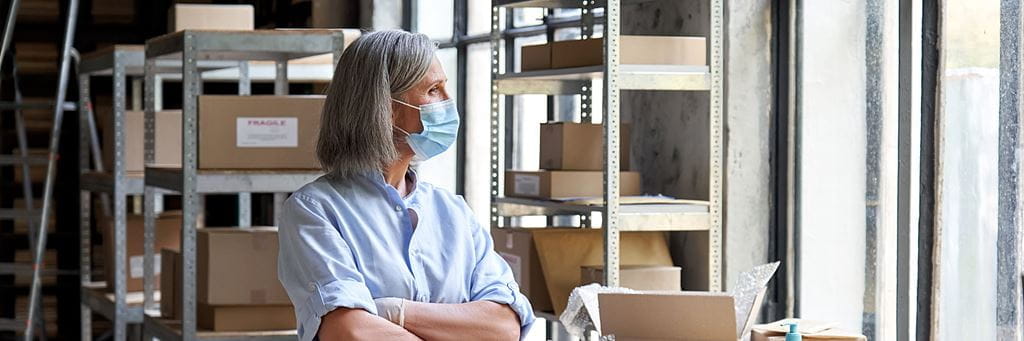 A woman business owner looks out the window in her company's stockroom.